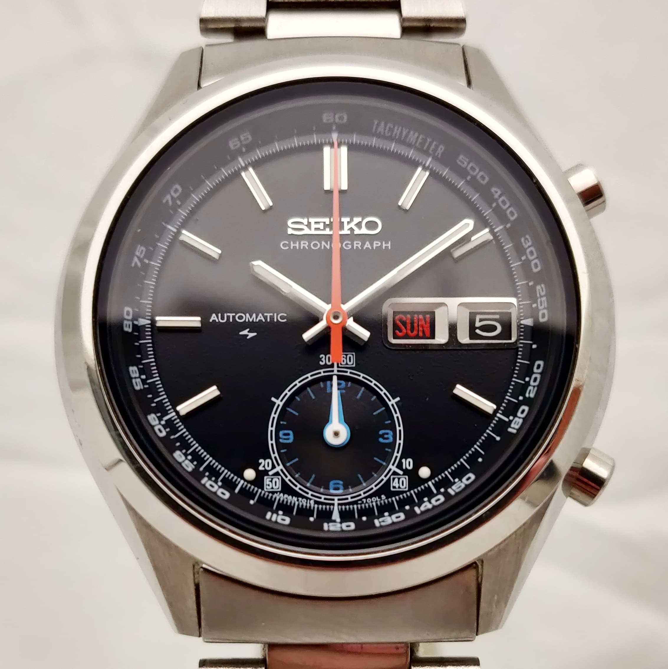 Reloj Seiko Chronograph automático en acero inoxidable con dial negro y detalles naranja y azul en Joyería Recoleta.